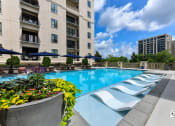 Thumbnail 34 of 58 - a swimming pool with lounge chairs and umbrellas in front of an apartment building