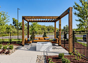 Thumbnail 26 of 29 - A wooden pergola with a bench and a fire pit in the middle of a garden.