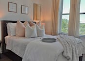 Thumbnail 26 of 32 - A bed with white pillows and a white blanket with a grey tray on it.