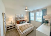 Thumbnail 14 of 23 - A bedroom with a large bed, a ceiling fan, and a window with blue curtains.