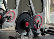 Thumbnail 13 of 32 - A stationary exercise bike with a red flywheel is in a room with a window.
