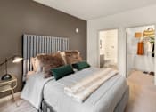 Thumbnail 5 of 27 - SE Redmond, WA, Pet-Friendly Apartments - The Bond - Bedroom with Carpet Flooring, Large Bed, Nightstand, Lamp, Oversized Closet, and Doorway Leading to the Bathroom.