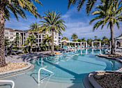 Thumbnail 2 of 54 - A pool surrounded by palm trees and a building in the background.