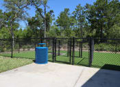 Thumbnail 21 of 24 - Luxury Apartments in Flagler Beach, FL, with In-Unit Washer and Dryer - Preserve at Flagler Beach - Gated Dog Park with Manicured Grass, Trash Can, and Surrounding Trees.