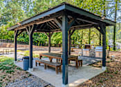 Thumbnail 31 of 35 - A wooden pavilion with a roof and four benches is situated in a park.