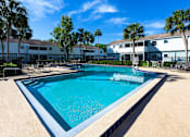 Thumbnail 1 of 25 - A large swimming pool surrounded by palm trees and buildings.
