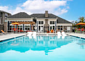 Thumbnail 1 of 24 - A large swimming pool in front of a house with a black fence and orange chairs.