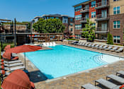 Thumbnail 20 of 46 - a swimming pool with chairs and umbrellas in front of an apartment building