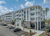 Thumbnail 36 of 47 - A large white apartment building with a parking lot in front.