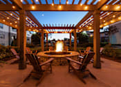Thumbnail 23 of 24 - A patio with a fire pit and chairs under a pergola.