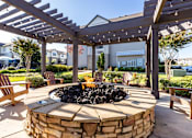 Thumbnail 2 of 24 - A backyard with a fire pit and wooden chairs under a pergola.
