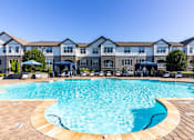 Thumbnail 1 of 24 - Two-Bedroom Luxury Apartments In Greenville, SC - The Aventine Greenville - A Large, Clear Blue Community Pool With Poolside Cabanas And Lounge Chairs In Front Of Stone-Accented Apartment Buildings.