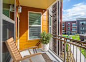 Thumbnail 7 of 36 - 2-Bedroom Apartments in Mt. Juliet, TN - The Enclave at Providence - A Balcony with an Orange Siding, Large Windows, Light Fixture, Wooden Lounge Chair, Brown Rug, Metal Railing, and Potted Plant.