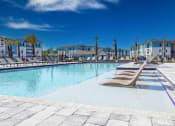 Thumbnail 15 of 24 - Pet-Friendly Luxury Apartments in Flagler Beach, FL - Preserve at Flagler - Sparkling Pool with In-Water Sun Shelf, Lounge Chairs, Palm Chairs, and View of Apartment Buildings.