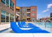 Thumbnail 27 of 32 - a pool with blue lounge chairs in front of an apartment building