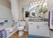 Thumbnail 13 of 18 - Apartments for Rent in Stockbridge, GA - Avenue 33 - Bathroom With a Large Vanity Mirror, White Cabinets, Wood-Inspired Plank Flooring, a Shower with Tub, and a Large Walk-In Closet with Carpet Flooring.