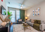 Thumbnail 26 of 46 - A living room with a grey couch, a coffee table, and a wall with framed pictures.