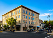 Thumbnail 1 of 25 - A large building with many windows sits on a street corner.