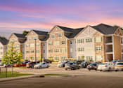 Thumbnail 1 of 31 - A large apartment complex with a parking lot in front.