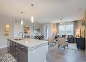 Thumbnail 7 of 37 - A modern kitchen with a large island and a dining area with a couch and chairs.