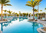 Thumbnail 1 of 54 - A large outdoor swimming pool surrounded by palm trees and lounge chairs.