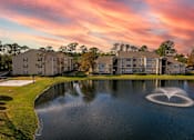Thumbnail 49 of 49 - A sunset view of a lake with a fountain in the middle and apartment buildings in the background.
