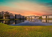 Thumbnail 46 of 49 - A serene landscape with a lake, grass, and buildings in the background.