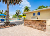 Thumbnail 16 of 26 - A yellow building with a stone wall and a palm tree in front at Coral Club Apartments in Bradenton, FL