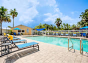 Thumbnail 17 of 26 - A pool area with sun loungers and a yellow building in the background at Coral Club Apartments in Bradenton, FL
