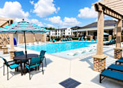 Thumbnail 25 of 35 - A pool area with a table and chairs and umbrellas.