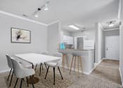 Thumbnail 11 of 29 - A white dining table with four chairs and a kitchen area in the background.