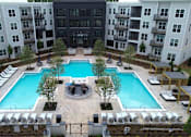 Thumbnail 1 of 28 - A large swimming pool surrounded by lounge chairs and trees in a courtyard.