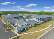 Thumbnail 1 of 28 - Huntsville, AL Luxury Apartments - The Kelvin - Aerial View of Property Exterior with White and Blue Walls, Grey Roofing, View of Pool, Surrounding Street, and Trees