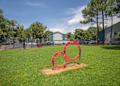 Thumbnail 27 of 30 - A red sculpture of three interlocking rings sits in a grassy field.