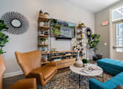 Thumbnail 5 of 30 - A living room with a brown leather chair, a blue sofa, and a coffee table with a vase of flowers on it.