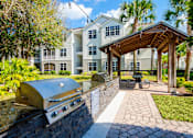 Thumbnail 25 of 36 - a patio with a grill and a picnic area with a building in the background