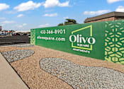 Thumbnail 28 of 28 - A green and white sign for Olivo Square Apartments with a phone number and website listed.