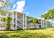 Thumbnail 12 of 15 - Two-Bedroom Luxury Apartments In Hollywood, FL - Park Hill Hollywood - An Exterior View Of A Three-Story White Apartment Building With External Staircases And A Lush Green Lawn Under A Blue Sky.