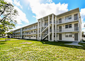 Thumbnail 11 of 15 - A white apartment building with a green lawn in front.