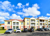 Thumbnail 15 of 15 - A row of cars parked in front of a multi-story apartment building.