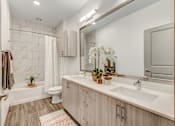 Thumbnail 18 of 30 - Dog-Friendly Luxury Apartments in Fort Worth, TX - The Union at River East - Bathroom with a White Bathtub, Wood-Style Flooring, Double-Sink Vanity, Large Mirror, Wall Cabinet, and Light Fixtures.