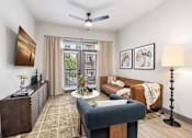 Thumbnail 5 of 43 - Duluth, GA, Apartments near Mercedes-Benz Stadium - District at Duluth - Living Room with Hardwood-Style Flooring, a Ceiling Fan, a Mounted TV, a Couch, and Doors to a Balcony.