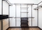 Thumbnail 14 of 43 - A black shelving unit with wire shelves and a black drawer is in a room with white walls.
