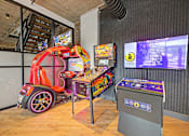 Thumbnail 40 of 43 - A red and black car-themed arcade game machine sits in a room with a wooden floor and a grey trash bin.