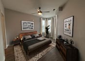 Thumbnail 15 of 36 - Two-Bedroom Apartments in Mt. Juliet, TN - The Enclave at Providence - Bedroom with Hardwood-Style Flooring, Large Bed, Dresser, Nightstands, Lamps, Wall Paintings, Ceiling Fan, and Large Windows.