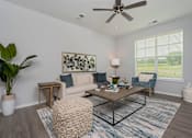 Thumbnail 7 of 35 - A living room with a white ceiling fan and a large window with blinds.
