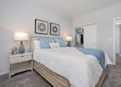 Thumbnail 5 of 14 - Dog-Friendly Luxury Apartments In Lebanon, OH - Founders Landing - A Modern Bedroom With A Light-Wood Bed, Blue Pillows And Lamps, And Geometric Wall Art.