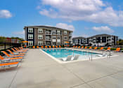 Thumbnail 27 of 35 - A swimming pool surrounded by orange lounge chairs in front of apartment buildings.