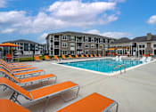 Thumbnail 29 of 35 - A swimming pool surrounded by orange sun loungers and a building in the background.