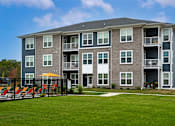 Thumbnail 32 of 35 - A large grey apartment building with a black fence in front.